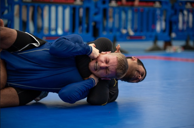 Two people in a no-gi BJJ match, one of them is in a Rear-Naked Choke but trying to fight it